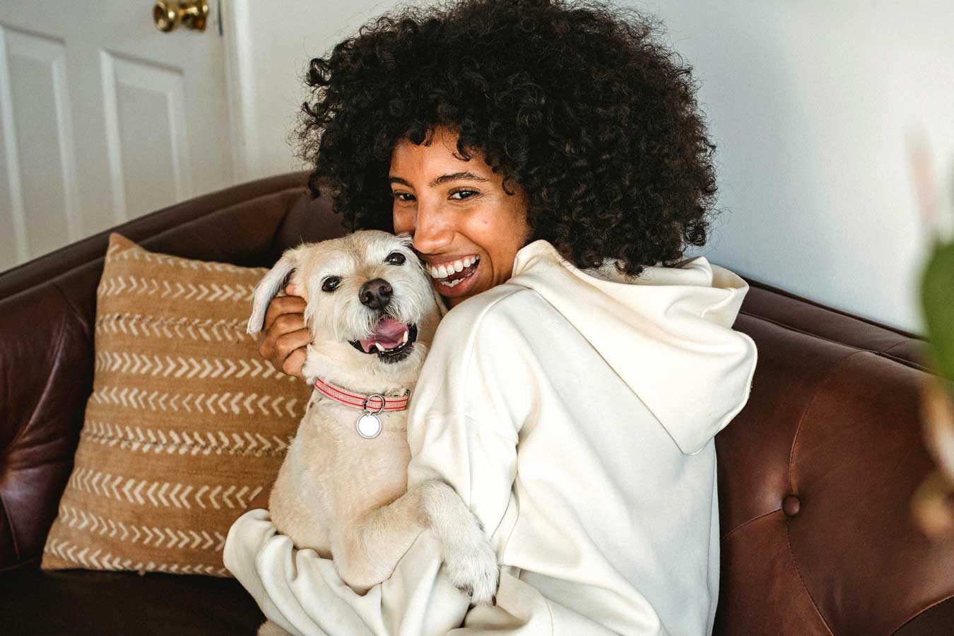A woman sits on her couch, cuddling a happy white dog.