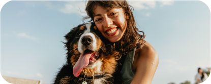 A woman smiles beside her Bernese Mountain Dog, who has its tongue out.
