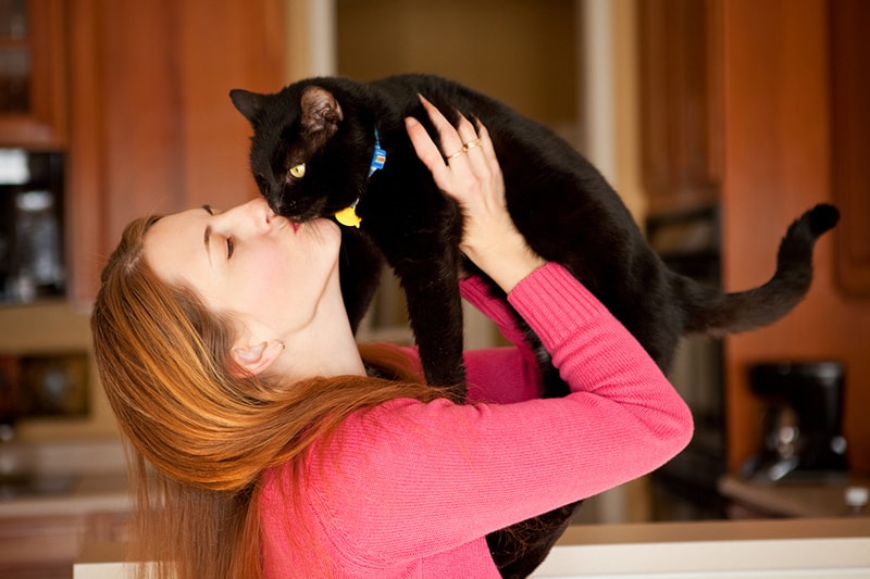 woman cuddling black cat 