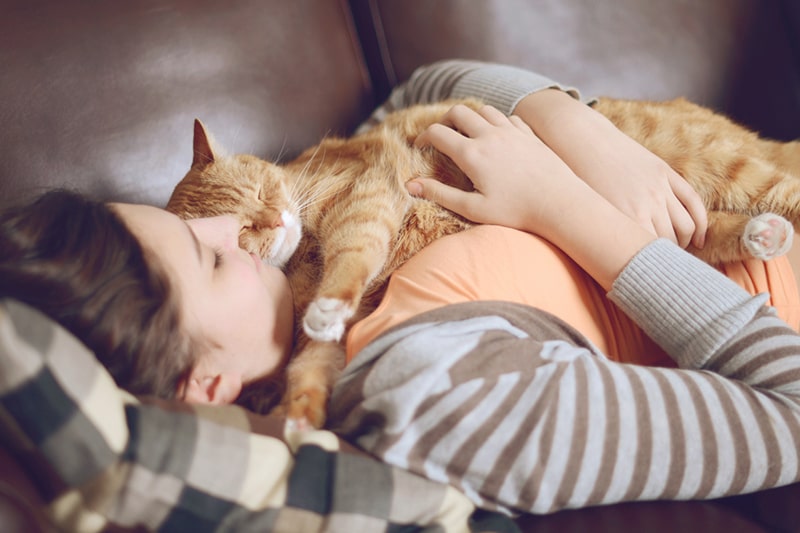 woman cuddling with an orange tabby cat on a brown leather sofa