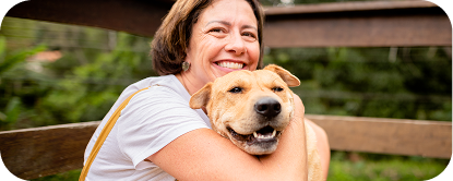 A woman sitting on a bench outdoors while holding a tan mixed-breed dog.