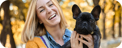 A woman outdoors holding a black French Bulldog.