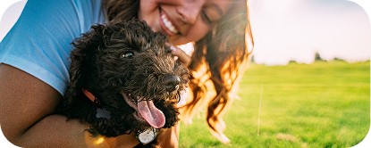 A woman outdoors hugs a black mixed-breed dog.