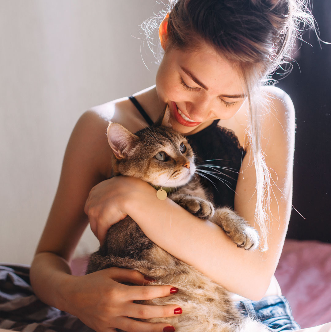 Smiling woman cuddles a tabby cat wearing a collar and ID tag.